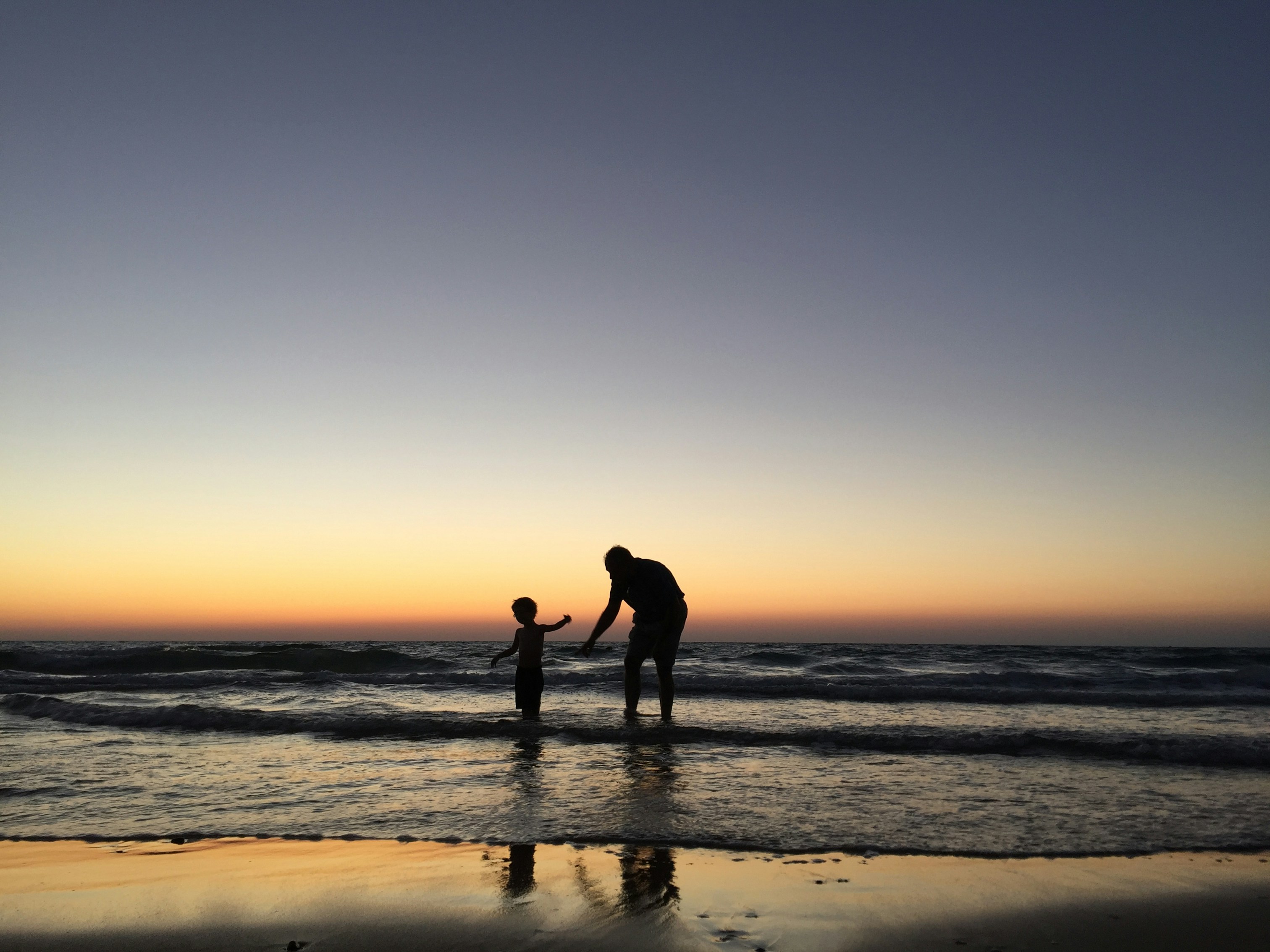 Adult and child playing in the surf at sunset